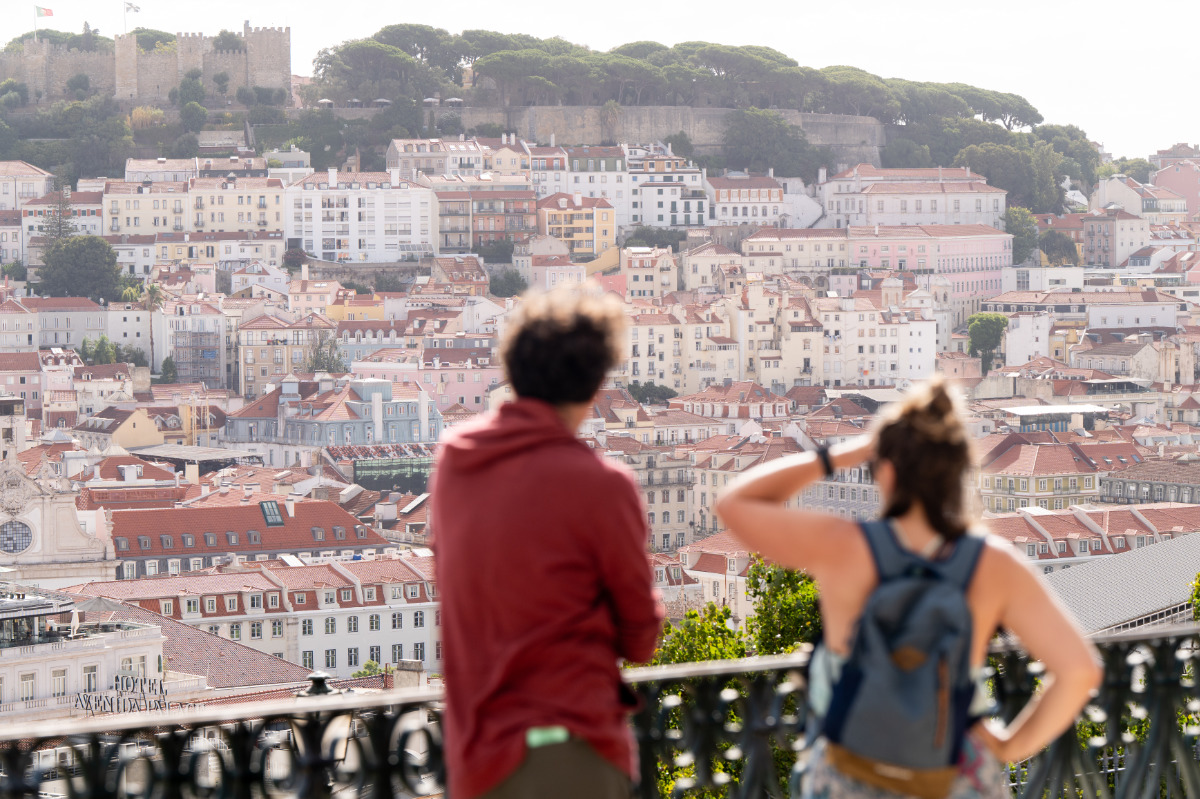 Casal a observar Lisboa no Miradouro de São Pedro de Alcântara, vendo-se o casario até à colina e Castelo de São Jorge