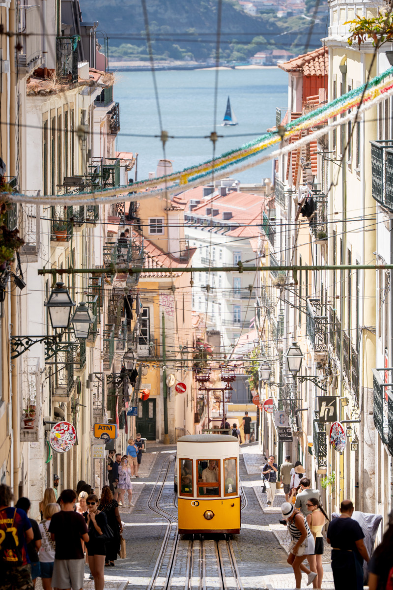 Elevador da Bica a subir a rua, com pessoas a caminhar pelos passeios laterais.
