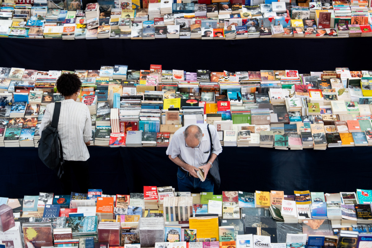 Pessoas a observar uma grande variedade de livros, entre três longas mesas numa feira literária.