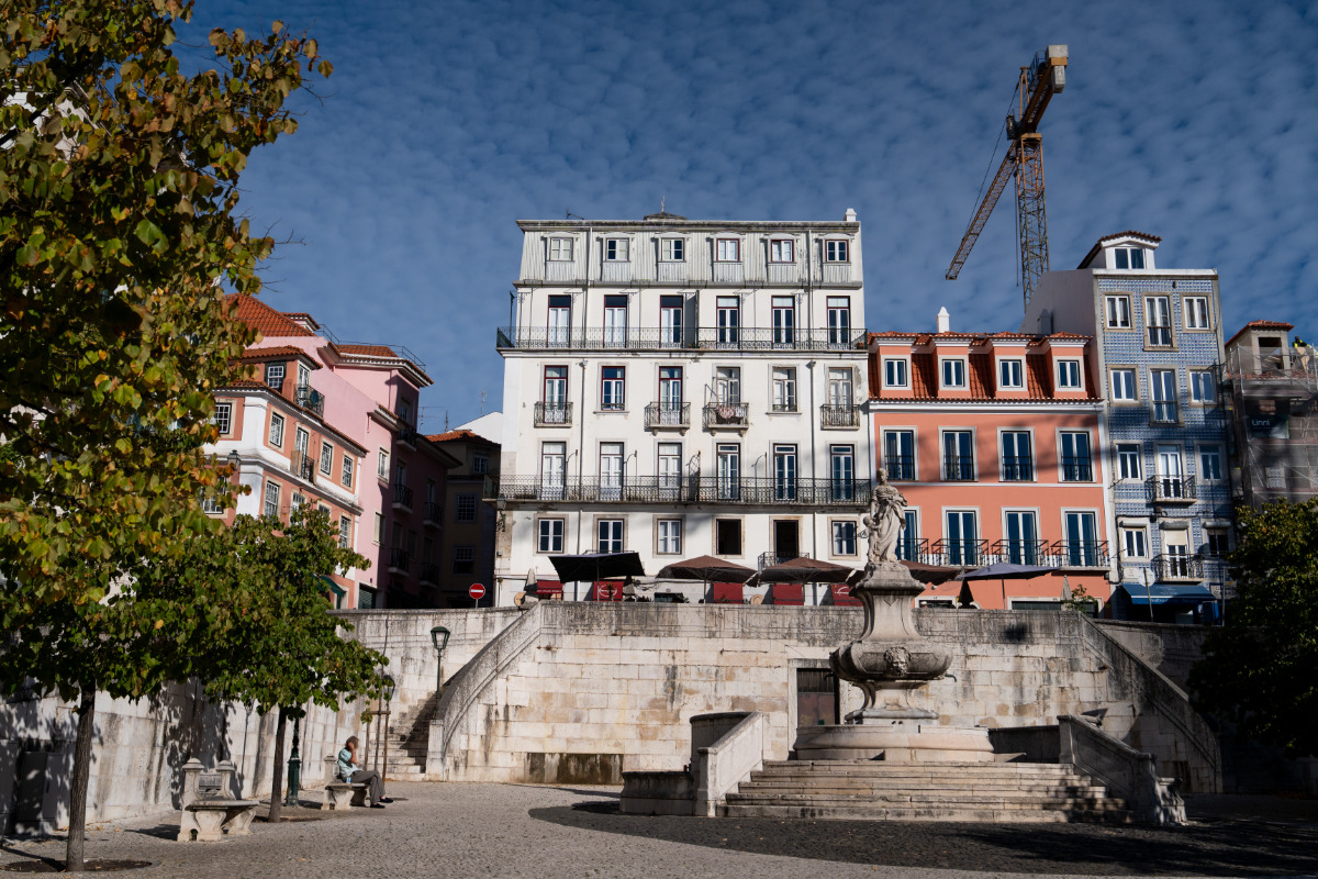Edifícios coloridos na colina da Lapa, e o largo onde se vê o Chafariz das Janelas Verdes e árvores ao redor, sob céu azul claro.