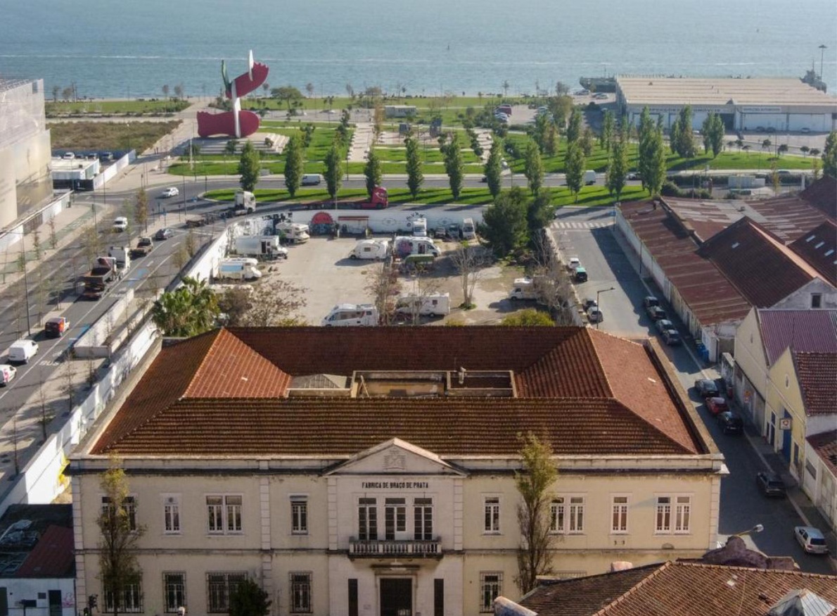 Vista aérea do edifício e área exterior da Fábrica Braço de Prata e, em segundo plano, espaço verde à beira do rio Tejo
