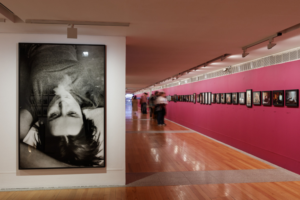 Sala do museu com vários quadros expostos na parede e pessoas a visitar a exposição