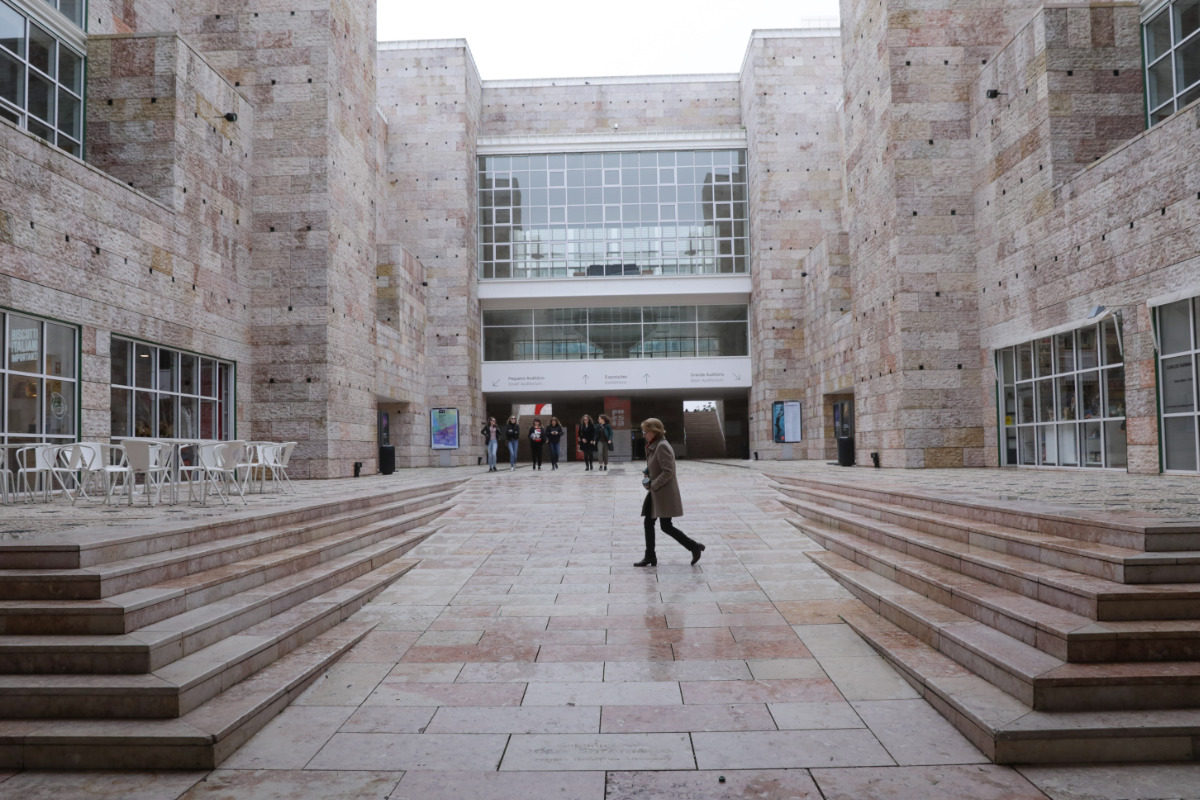 Pátio central do Centro Cultural de Belém, com escadarias laterais em pedra, edifícios revestidos a calcário e pessoas a circular no espaço.