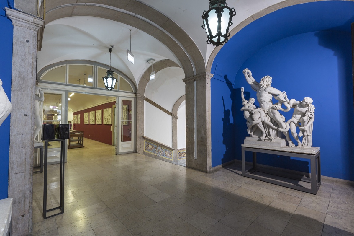 Entrada do convento, com teto abobadado, uma parede azul e uma escultura branca proeminente.
