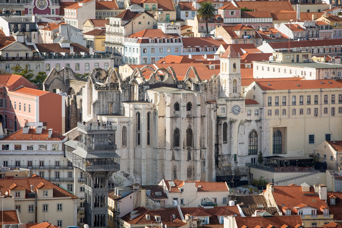 Uma vista panorâmica de Lisboa mostrando as ruínas do Convento do Carmo rodeado por edifícios coloridos com telhados vermelhos.