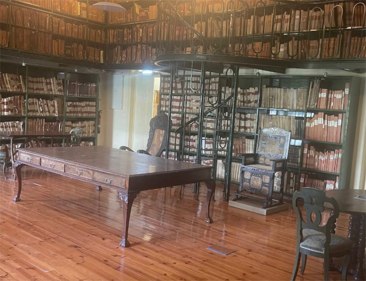 Fotografia de uma sala do Arquivo Histórico Ultramarino, com dois pisos, uma escada caracol e paredes repletas de estantes de livros e documentos antigos.