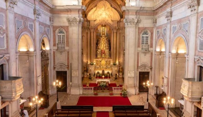 Interior da Igreja de São Nicolau com altar central decorado, detalhes ornamentais em estilo barroco, iluminação suave e assentos de madeira.