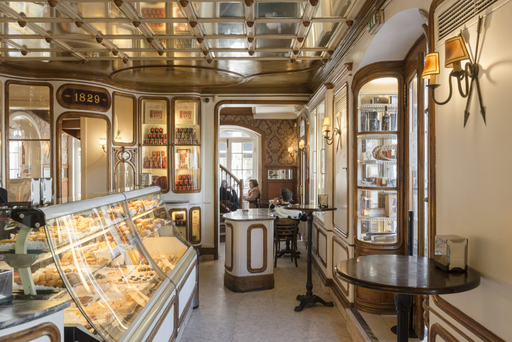 Interior elegante da Confeitaria Nacional com decoração vintage, com uma vitrine repleta de doces variados. A iluminação acolhedora e os tons ricos da madeira criam um ambiente aconchegante.