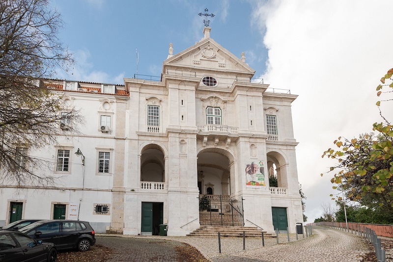 Fotografia da fachada da Igreja de Nossa Senhora da Penha de França, com entrada arqueada, colunas e cruz no topo. O edifício possui várias janelas com molduras ornamentadas e um design simétrico.