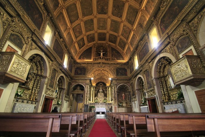 Interior da Igreja dos Anjos com detalhes em ouro, bancos de madeira e arquitetura barroca, destacando-se pelo peso cultural e artístico.