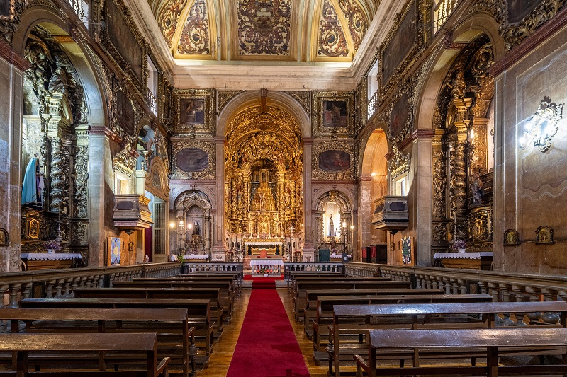 Interior da Igreja de São Miguel com altar dourado, paredes decoradas detalhadamente e bancos de madeira, destacando-se pela sua arquitetura clássica e ornamentação luxuosa.