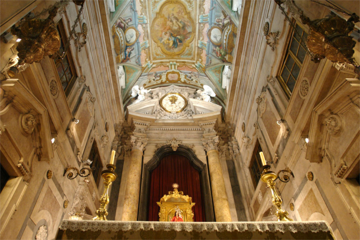 Interior da Basílica dos Mártires, ornamentado - teto com frescos, colunas, altar dourado, cortina vermelha e dois grandes castiçais no altar.