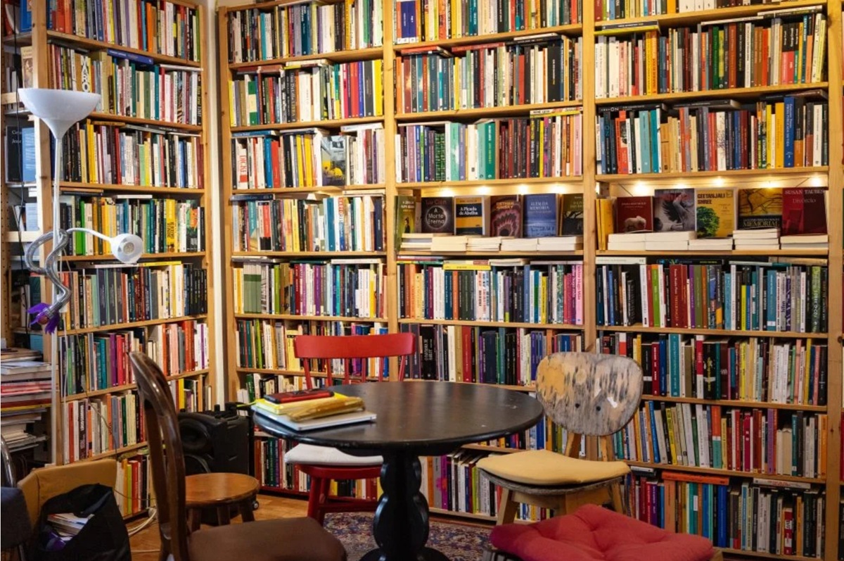 Interior da livraria Snob, com várias estantes repletas de livros, uma mesa redonda no centro com alguns livros empilhados e cadeiras ao redor, criando um ambiente acolhedor e literário.