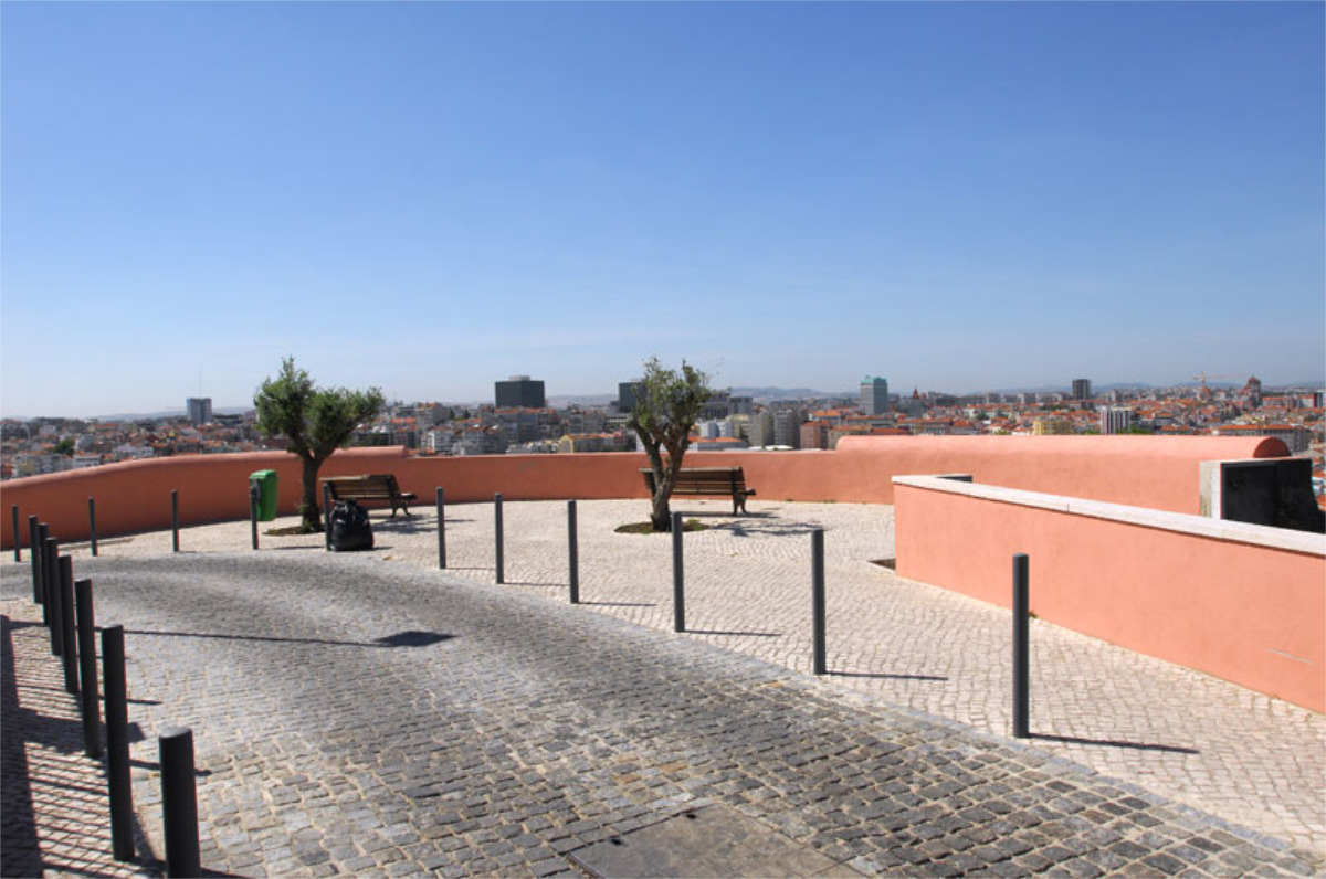 Miradouro com ampla vista da cidade de Lisboa, com bancos, árvores, piso de pedra e delimitado por baixo muro cor-de-rosa.